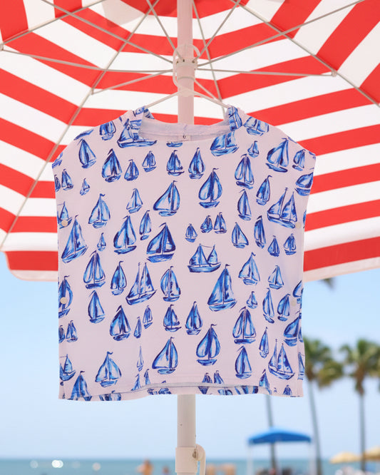 Blue sailboats-patterned towel poncho hanging on a wooden branch with greenery in the background