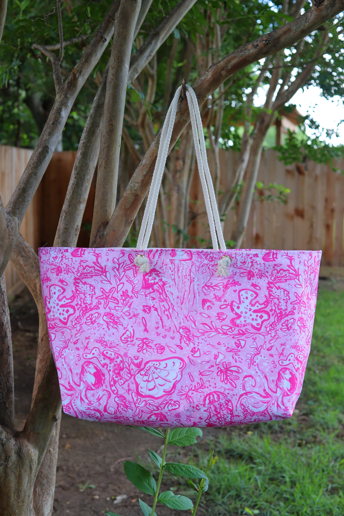 Pink patterned tote bag hanging on a tree branch outdoors
